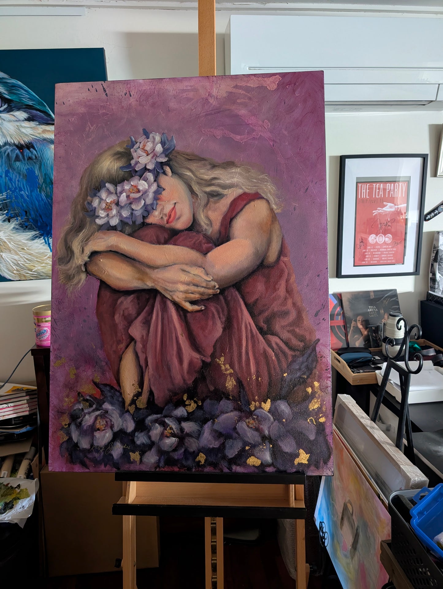 Blooming Through the Night showing the woman’s face, flowers, folded arms and textured mixed media surface in the studio on the easel. Newly varnished.