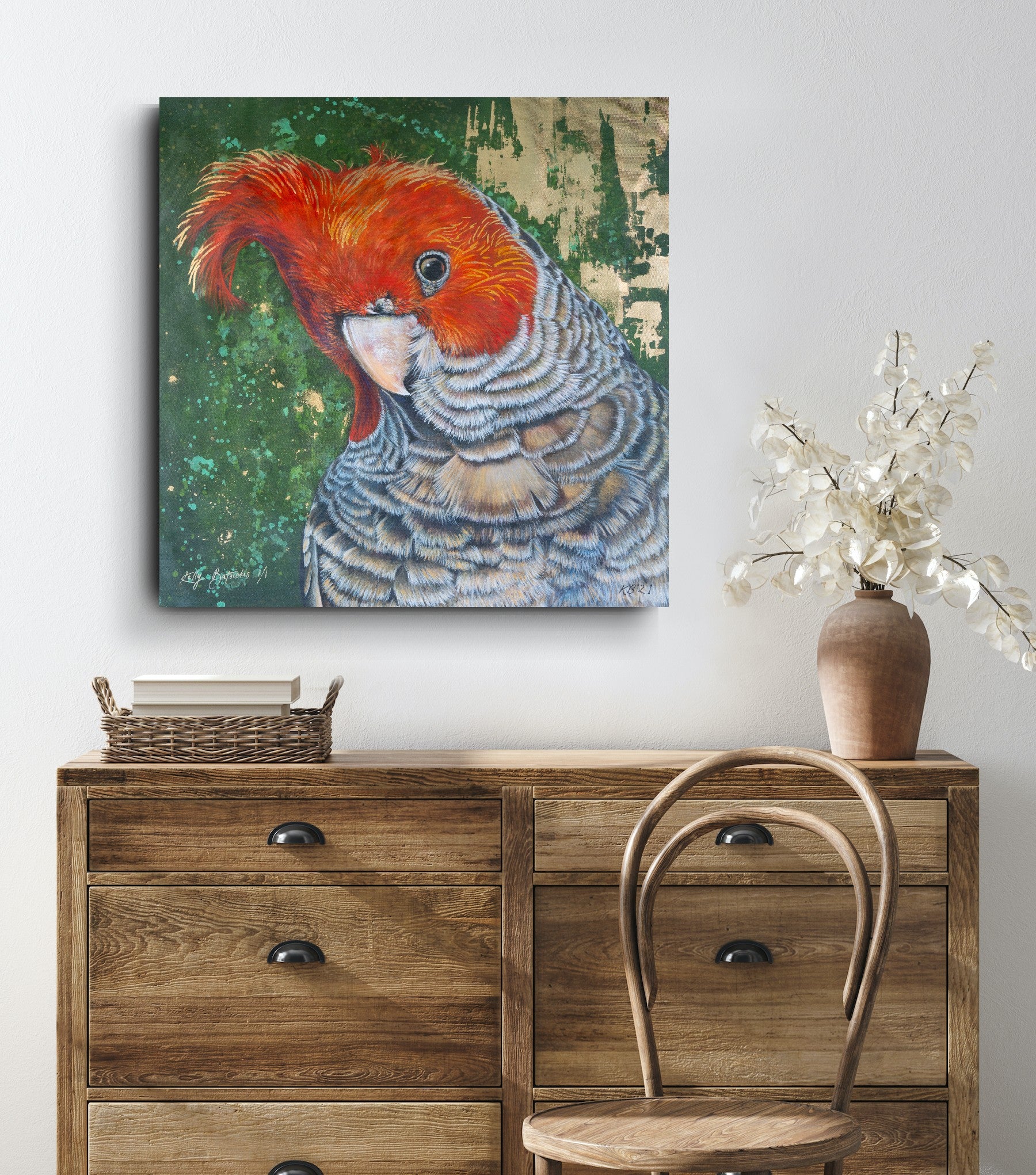 Unframed, embellished fine art print of Elvis the Gang Gang Cockatoo by Kelly Batsiokis on a wall above a wooden console table with a chair and vase to show scale. Please note the 91cm print is transported rolled and will require stretching for presentation/ hanging. Future prints of this nature are also unlikely to have embellishment on the feature bird (just in the background - in more of a halo feature like the 30cm version).