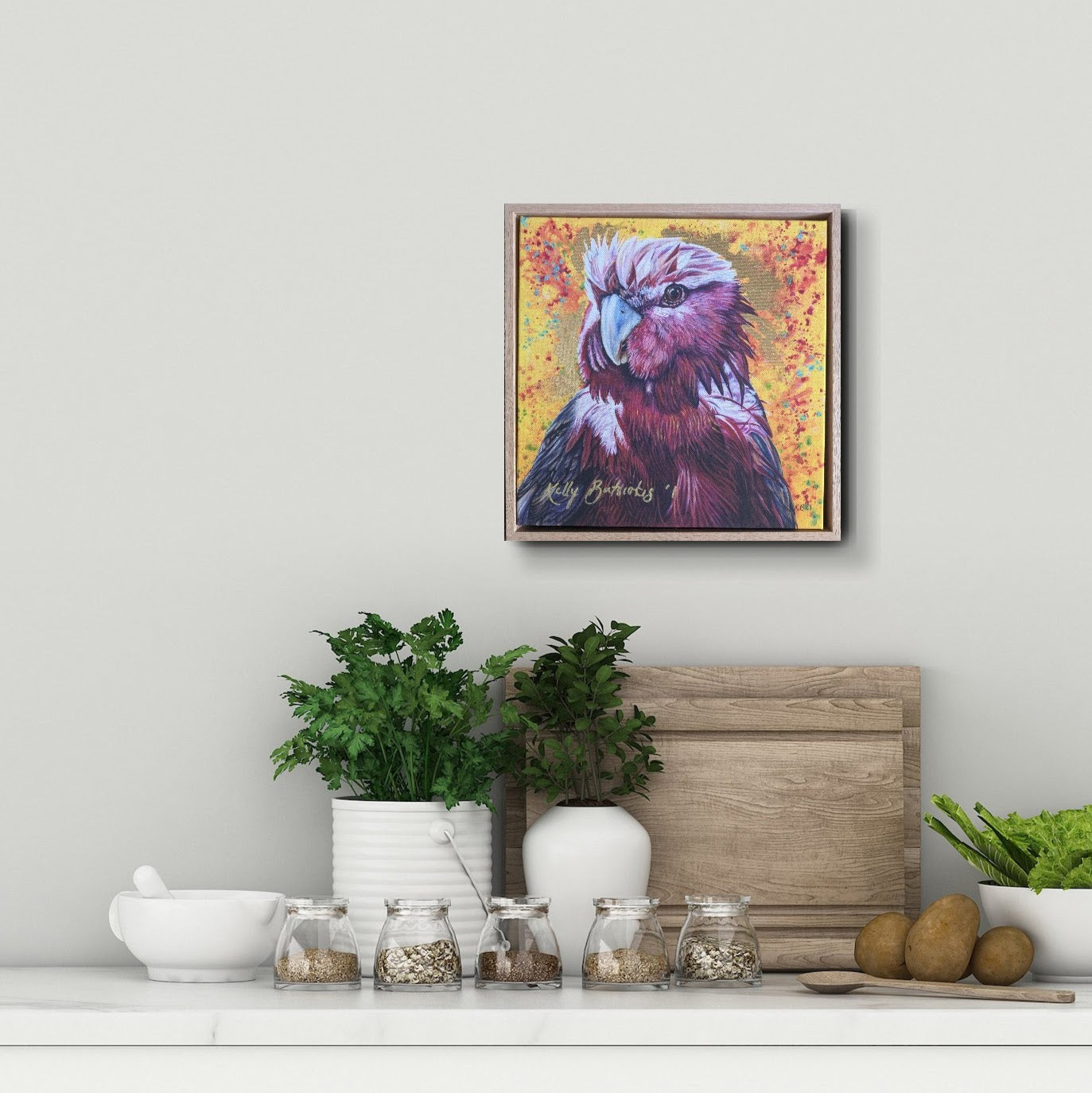 Framed embellished fine art print of Wally the Galah by Kelly Batsiokis on a textured fabric background to scale against a styled kitchen shelf backdrop.
