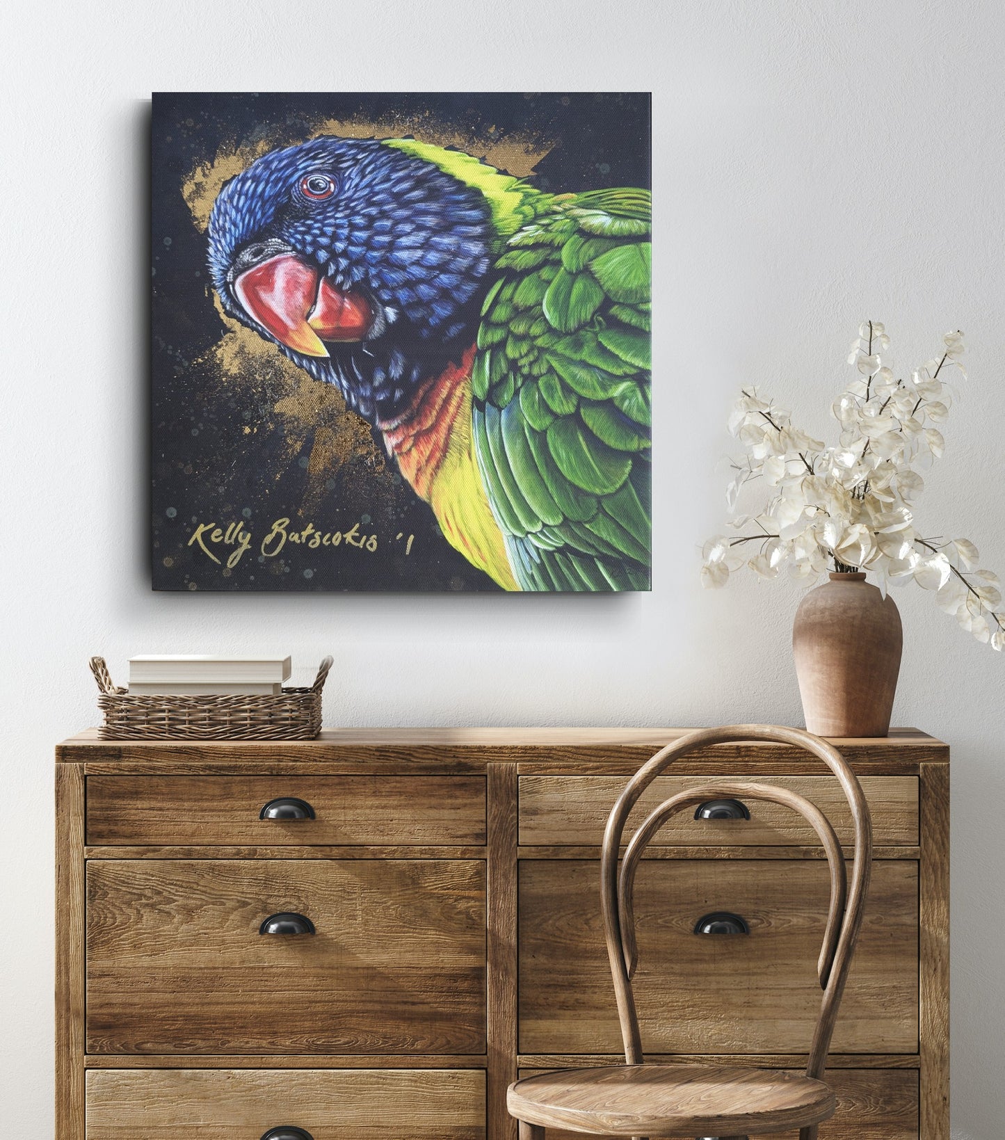 Unframed fine art embellished print of Shazza the Rainbow Lorikeet on a wall above a wooden dresser with a chair and vase to show scale. Please note that the  91cm print is purchased rolled and will require stretching and/or framing for presentation/hanging. The signature will also not be so large (the smaller version has been enlarged for illustrative purposes to show scale).