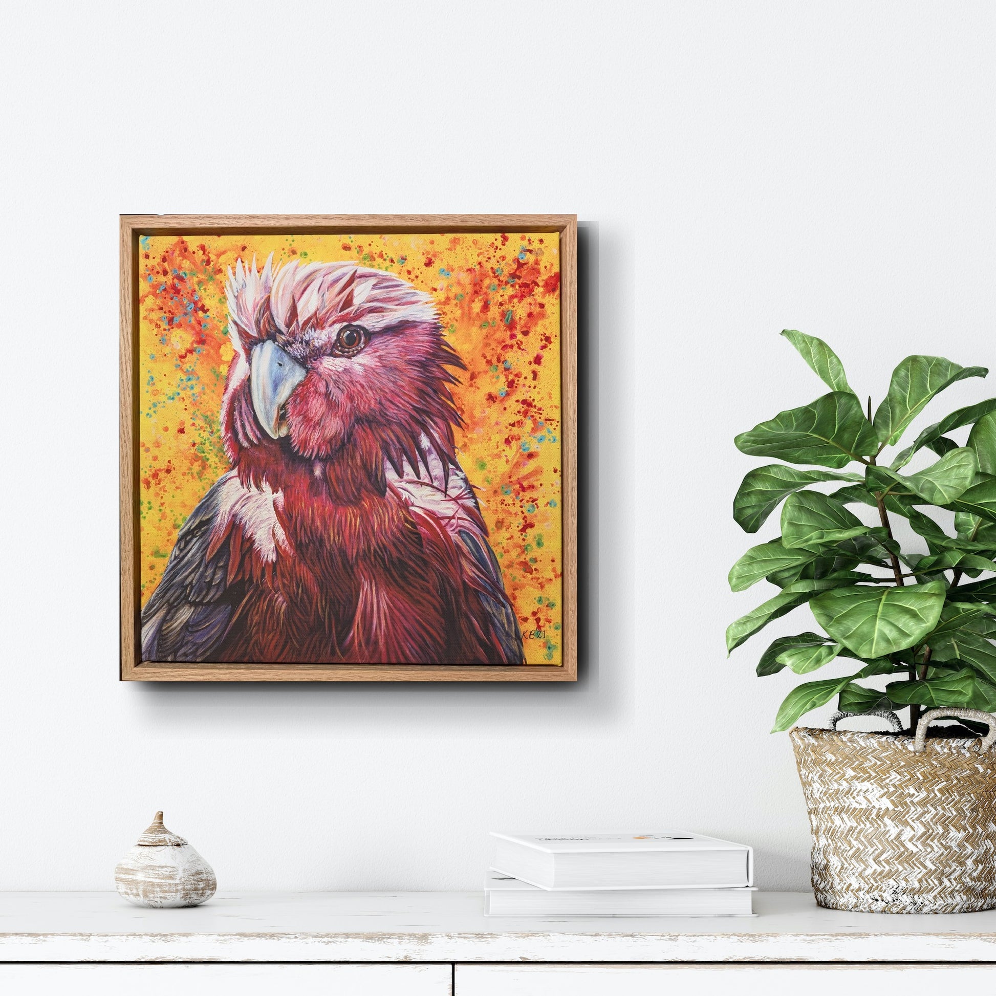 Framed fine art print of Wally the Galah painting on a wall above a white surface with decor items to show scale.