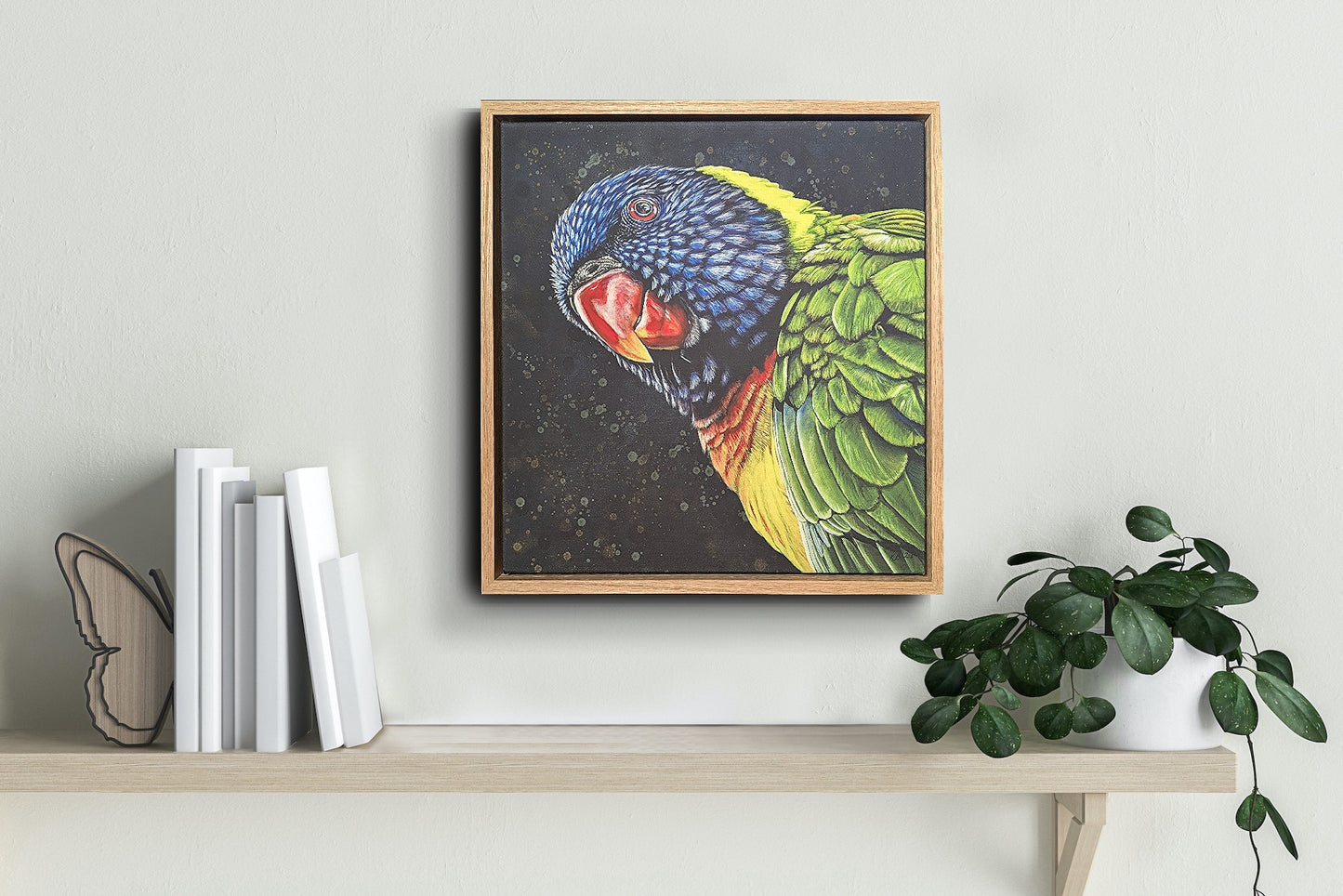 Framed fine art reproduction print of Shazza the Rainbow Lorikeet by Kelly Batsiokis on a shelf with books and a plant to show scale.