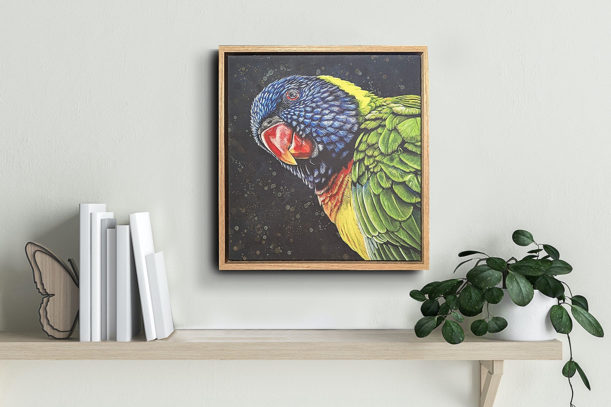 Framed fine art reproduction print of Shazza the Rainbow Lorikeet by Kelly Batsiokis on a shelf with books and a plant to show scale.