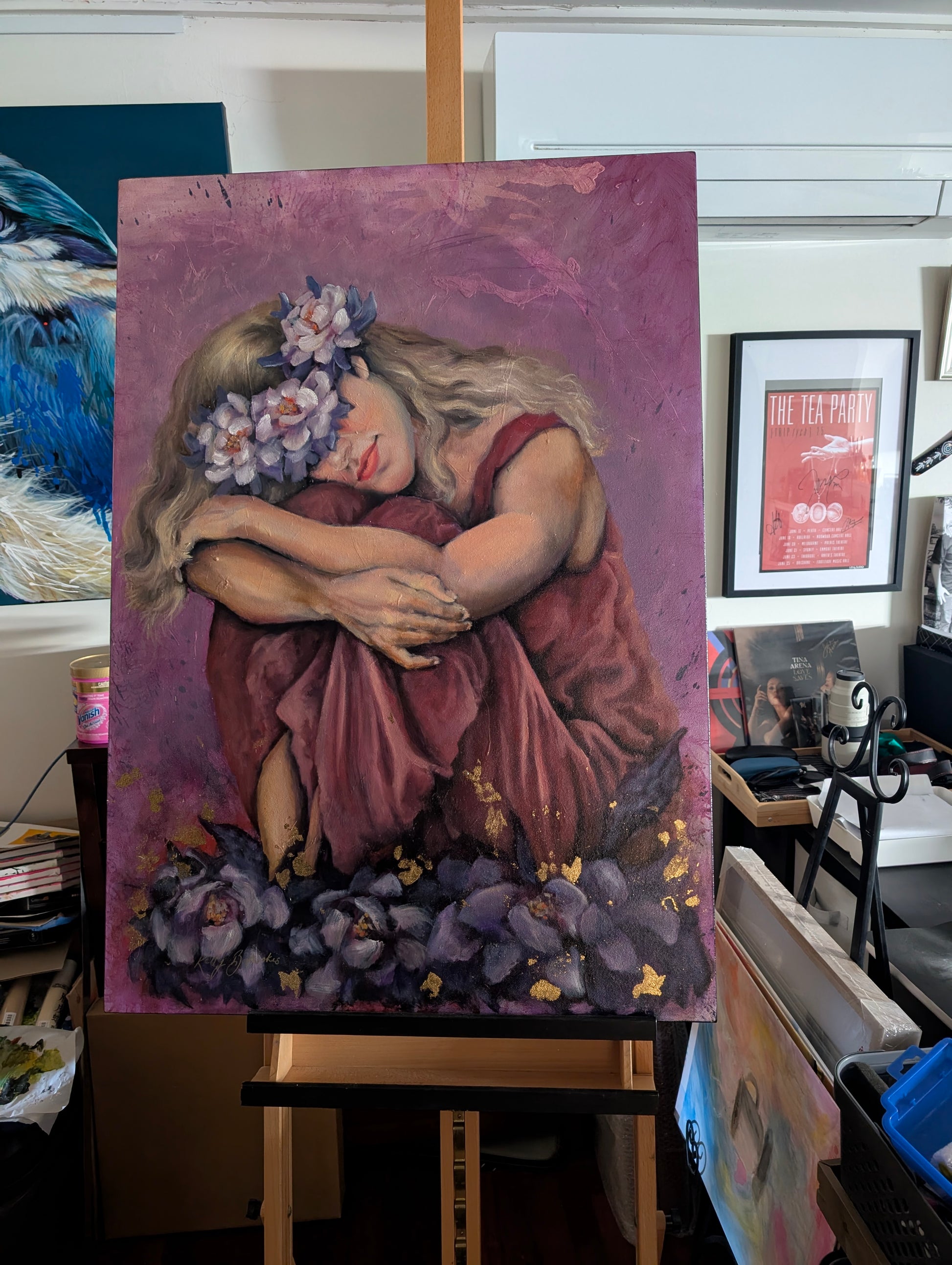 Blooming Through the Night showing the woman’s face, flowers, folded arms and textured mixed media surface in the studio on the easel. Newly varnished.